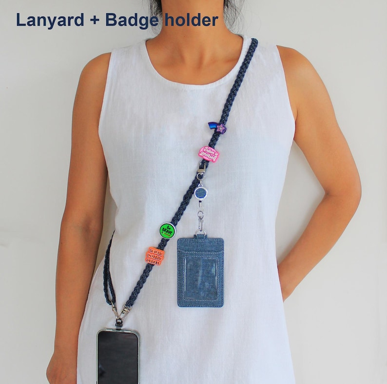 May include: A dark blue braided lanyard featuring multiple colorful pins, a retractable badge reel, and a denim-textured badge holder. The lanyard includes a metal clip for a phone and the text Lanyard + Badge holder is visible.