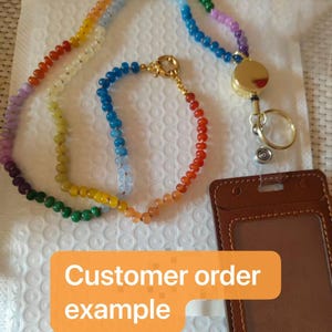 Puede incluir: Un cord&oacute;n con una larga hilera de cuentas multicolores en degradado de arco&iacute;ris, conectado a un carrete de insignia retr&aacute;ctil dorado con una anilla met&aacute;lica. Incluye un portaidentificaci&oacute;n vertical de piel sint&eacute;tica marr&oacute;n con el texto Customer order example.
