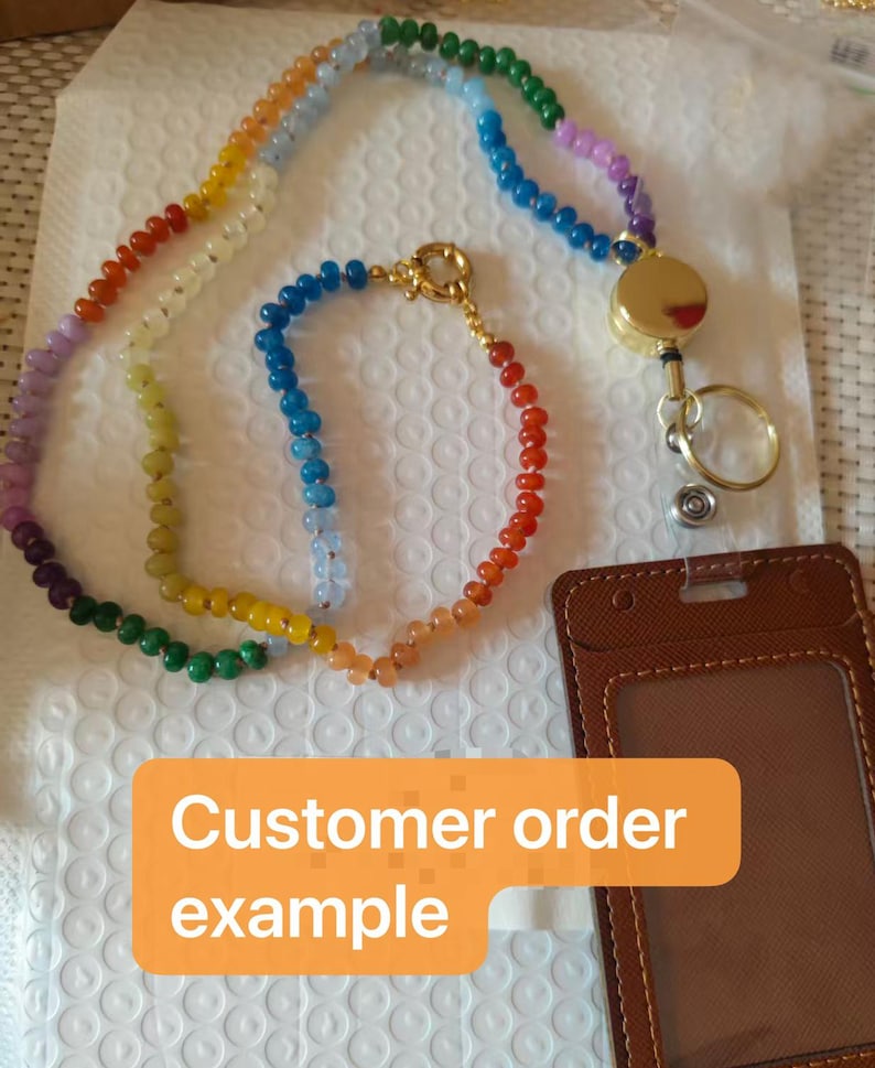 Puede incluir: Un cord&oacute;n con una larga hilera de cuentas multicolores en degradado de arco&iacute;ris, conectado a un carrete de insignia retr&aacute;ctil dorado con una anilla met&aacute;lica. Incluye un portaidentificaci&oacute;n vertical de piel sint&eacute;tica marr&oacute;n con el texto Customer order example.