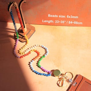 Puede incluir: Un cord&oacute;n de cuentas multicolor con cuentas de 6x3mm y una longitud total de 84-88cm. El cord&oacute;n incluye un carrete retr&aacute;ctil dorado, un mosquet&oacute;n, una anilla para llaves y un tarjetero de color marr&oacute;n con textura para identificaci&oacute;n.