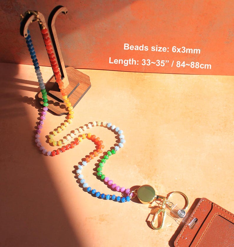 Puede incluir: Un cord&oacute;n de cuentas multicolor con cuentas de 6x3mm y una longitud total de 84-88cm. El cord&oacute;n incluye un carrete retr&aacute;ctil dorado, un mosquet&oacute;n, una anilla para llaves y un tarjetero de color marr&oacute;n con textura para identificaci&oacute;n.