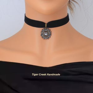 May include: Black velvet choker necklace with a decorative pendant. The pendant is a square shape surrounded by small, clear crystals. The text "Tiger Creek Handmade" is at the bottom of the image.