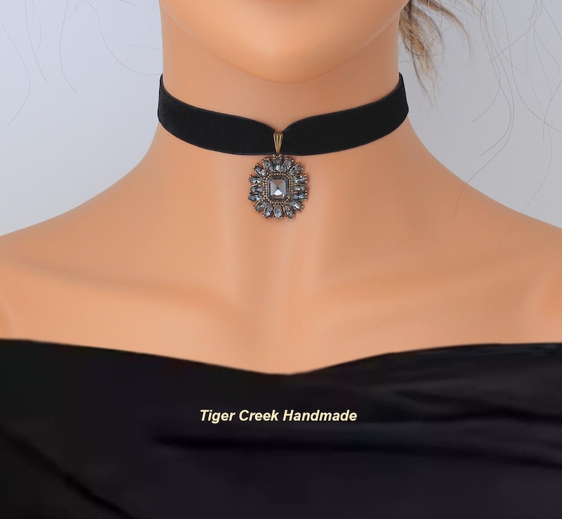 May include: Black velvet choker necklace with a decorative pendant. The pendant is a square shape surrounded by small, clear crystals. The text "Tiger Creek Handmade" is at the bottom of the image.