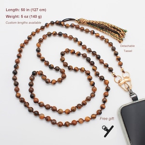 May include: A beaded lanyard made of brown and gold tiger eye stones, measuring 50 inches in length and weighing 5 ounces. It features a detachable multi-colored tassel, a gold-toned metal clasp, and a black phone attachment component.
