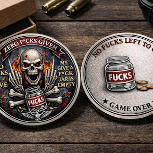 Könnte beinhalten: Zwei silberfarbene Challenge-Münzen. Eine Münze zeigt einen Schädel mit Flammen, Knochen und dem Text "ZERO F*CKS GIVEN". Die andere Münze zeigt ein Glas mit der Aufschrift "FUCKS" und dem Text "NO FUCKS LEFT TO GIVE" und "GAME OVER".