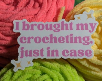 May include: A white die-cut sticker with pink text that reads I brought my crocheting, just in case, accented with small gold star icons. The sticker is positioned against a background of bright pink, yellow, and lime green yarn balls.