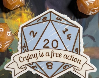May include: A light blue sticker shaped like a twenty-sided die with brown outlines and numbers. A white banner across the center features the brown text "Crying is a free action." The sticker is surrounded by five translucent orange dice.