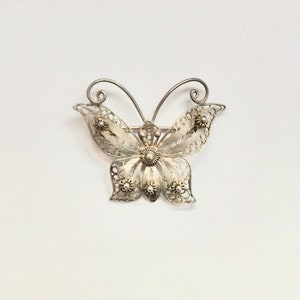 May include: A silver filigree butterfly brooch with a detailed design. The butterfly has a delicate, intricate pattern and is a beautiful piece of jewelry.
