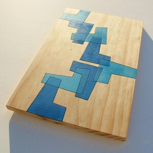 May include: A wooden cutting board with a blue geometric design. The design is made up of various shapes and sizes of blue squares and rectangles.