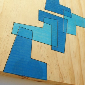 May include: Abstract geometric design painted on a light wood surface. The design is made up of overlapping blue shapes.