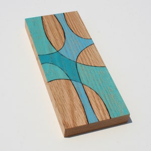 May include: A wooden wall art piece with a geometric design in shades of blue and teal. The wood has a natural grain pattern.