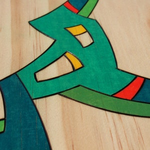 Puede incluir: Primer plano de una superficie de madera con un dise&ntilde;o abstracto en verde, azul, amarillo y rojo. El dise&ntilde;o est&aacute; hecho de madera incrustada y tiene un contorno negro.
