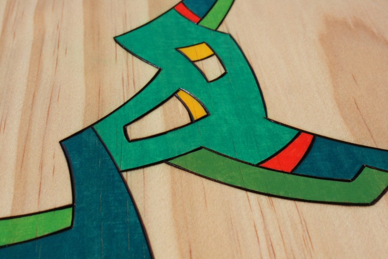 Puede incluir: Primer plano de una superficie de madera con un dise&ntilde;o abstracto en verde, azul, amarillo y rojo. El dise&ntilde;o est&aacute; hecho de madera incrustada y tiene un contorno negro.