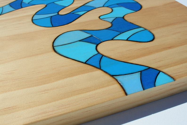 May include: Wooden art piece featuring a flowing river design in shades of blue. The river is composed of geometric shapes and is set against a light-colored wood background. The artwork has a glossy finish and a modern aesthetic.