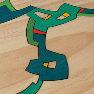 Puede incluir: Dise&ntilde;o abstracto sobre una superficie de madera. El dise&ntilde;o est&aacute; formado por formas de color turquesa, verde, amarillo y rojo.