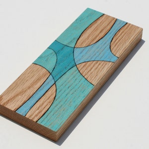 May include: A rectangular wooden wall art piece with a blue and brown abstract design. The wood is stained a light brown and the blue design is painted on top. The design is made up of curved lines and circles.