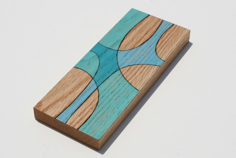 May include: A rectangular wooden wall art piece with a blue and brown abstract design. The wood is stained a light brown and the blue design is painted on top. The design is made up of curved lines and circles.