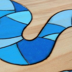 May include: Close-up of a wooden surface with a blue, abstract design. The design is composed of various shades of blue, from light to dark, with black outlines. The design has a flowing, curved shape.