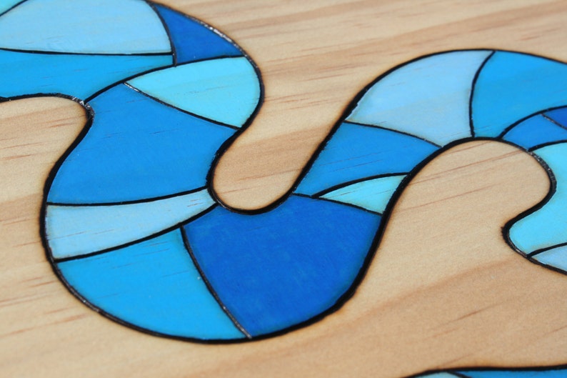 May include: Close-up of a wooden surface with a blue, abstract design. The design is composed of various shades of blue, from light to dark, with black outlines. The design has a flowing, curved shape.