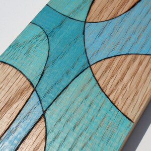 May include: A wooden board with a geometric design painted in shades of blue. The design is made up of curved lines and shapes.