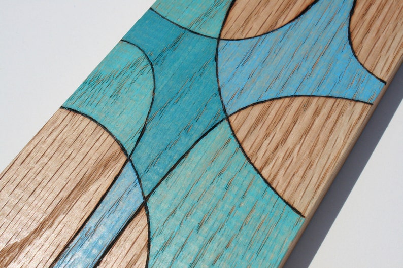 May include: A wooden board with a geometric design painted in shades of blue. The design is made up of curved lines and shapes.