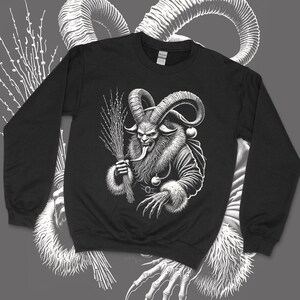 May include: Black sweatshirt featuring a detailed white illustration of a Krampus figure. The design includes a horned demon with a long tongue, holding a bundle of birch branches. The sweatshirt has a crew neck and long sleeves.
