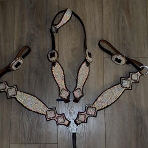 May include: A horse bridle and breast collar set. The set features brown leather with silver-toned hardware and is embellished with sparkling rhinestones. The breast collar has a central silver-toned decorative piece.