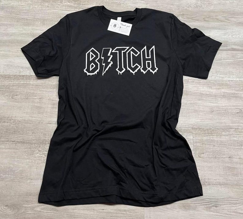Pode incluir: Camiseta preta com um gr&aacute;fico branco da palavra "BITCH" em uma fonte de metal que pinga com um raio.