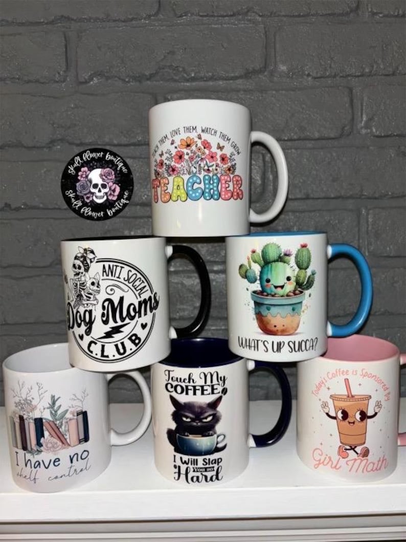 May include: A collection of 7 ceramic mugs with various designs and text. The mugs are white with black, blue, pink, and green accents. The text on the mugs includes "Teacher", "Anti Social Dog Moms Club", "What's Up Succa?", "Touch My Coffee", "I Will Slap You So Hard", "I Have No Shelf Control", and "Today's Coffee Is Sponsored By Girl Math".