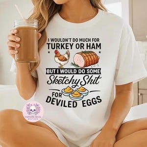 May include: White t-shirt with the text "I wouldn't do much for turkey or ham, but I would do some sketchy shit for deviled eggs." The graphic includes a chicken, a ham, and deviled eggs.