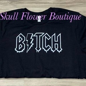 Pode incluir: Camiseta preta com um gr&aacute;fico branco que diz "B*TCH" em uma fonte g&oacute;tica que pinga.