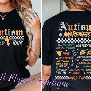Peut inclure: T-shirt noir avec un motif graphique coloré qui dit "Autism Awareness World Tour" et comprend un éclair et un motif à carreaux. Le dos du t-shirt comporte une liste de phrases liées à la sensibilisation à l'autisme, notamment "Voir la capacité, pas le handicap", "L'amour n'a pas besoin de mots", "Penser différemment", "Soyez gentil", "Tout le monde communique différemment", "Une personne, pas un puzzle", "Neurodiversité", "L'acceptation est un choix", "L'inclusion compte".