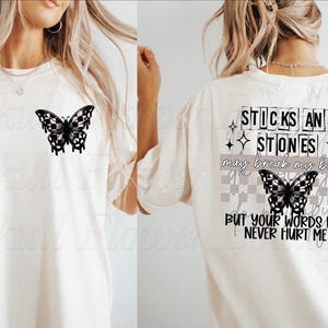 Puede incluir: Una camiseta blanca con un gráfico de mariposa negra en la parte delantera y el texto "Sticks and stones may break my bones but your words will never hurt me" en la parte posterior.