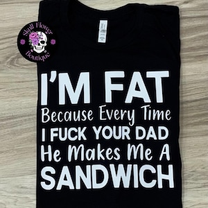 May include: A black short-sleeved t-shirt with white text that reads I'M FAT Because Every Time I FUCK YOUR DAD He Makes Me A SANDWICH. A circular logo in the top left corner features a white skull with pink flowers and the text Skull Flower Boutique.