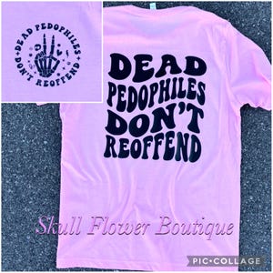 Może przedstawiać: Różowa koszulka z czarnym napisem "Dead Pedophiles Don't Reoffend". Tekst jest w stylu retro. Koszulka jest dostępna w sklepie Skull Flower Boutique.