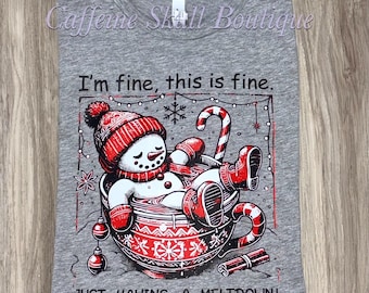 Può includere: T-shirt grigio melange con grafica di un pupazzo di neve in una tazza rossa e bianca, con cappello e guanti. Il testo recita: "I'm fine, this is fine. JUST HAVING A MELTDOWN!" La maglietta è di Caffeine Skill Boutique.