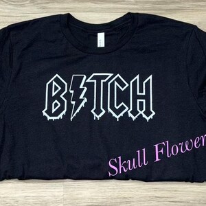 Pode incluir: Camiseta preta com um gr&aacute;fico branco que diz "B*TCH" em uma fonte de metal que pinga.