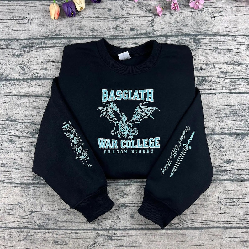 May include: Black sweatshirt with the text "BASGIATH WAR COLLEGE DRAGON RIDERS" in a light blue font. A dragon graphic is centered above the text. The left sleeve has a light blue design, and the right sleeve has a sword graphic and the text "Violent Little Thing".