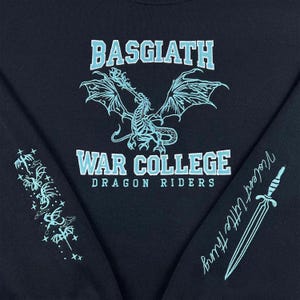 May include: Black sweatshirt with light blue text and graphics. The front features a dragon design and the words "BASGIATH" and "WAR COLLEGE DRAGON RIDERS." The left sleeve has a floral design, and the right sleeve has a sword and the words "Violent Little Thing."