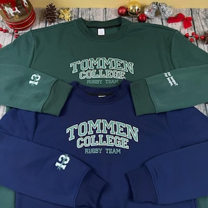 May include: Two sweatshirts, one dark green and one navy blue, are displayed. Both have the text "TOMMEN COLLEGE RUGBY TEAM" in white and green. The green sweatshirt has the number "13" on the left sleeve and the words "For keeps? For keeps." on the right sleeve.