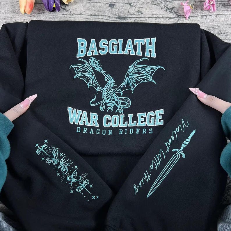 May include: Black sweatshirt with "BASGIATH WAR COLLEGE DRAGON RIDERS" text and a dragon graphic in light blue. The left sleeve has a floral design, and the right sleeve has a dagger and the text "Violent Little Thing".