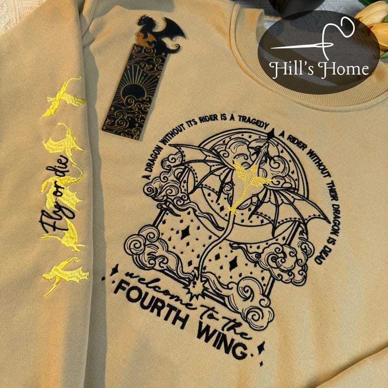 May include: A beige sweatshirt with black embroidered text that reads "A dragon without its rider is a tragedy. A rider without their dragon is dead. Welcome to the Fourth Wing." The text is surrounded by an embroidered image of a dragon with wings outstretched. The sweatshirt has yellow embroidered text on the sleeves that reads "Fly or die."