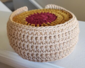 Op de afbeelding: Een gehaakte set onderzetters met een beige buitenlaag en een meerkleurige binnenlaag. De binnenlaag heeft een rood midden omgeven door geel en oranje.