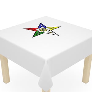May include: White tablecloth with a five-pointed star design in the center. The star is outlined in black and has a yellow, green, blue, and red point. The star has a small gold symbol in the center.