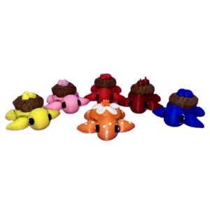 May include: Six small turtle figurines, each with a different colored shell and a small decorative element on top. The turtles are yellow, pink, orange, red, blue, and brown.