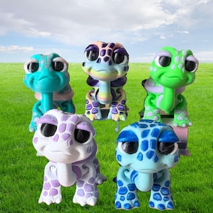 Puede incluir: Cinco pequeñas figuritas de tortugas con caparazones coloridos y estampados y grandes ojos expresivos. Las tortugas están pintadas en tonos de azul, verde, morado y blanco.