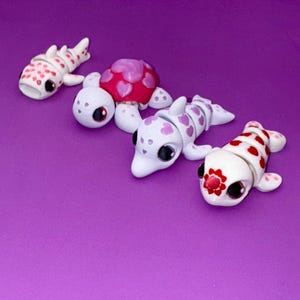 May include: Four small white figurines of sea creatures with pink and red hearts. The figurines are a shark, a turtle, a dolphin, and a fish.