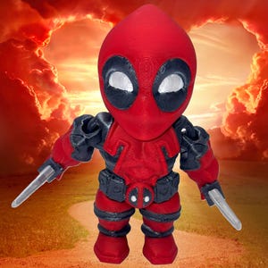 May include: A red and black 3D printed figurine of Deadpool, a superhero character, with two swords. The figurine is standing on a path with a red and orange cloudy sky in the background.