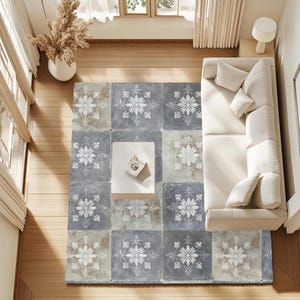 May include: Overhead view of a living room with a patterned rug. The rug is composed of square tiles in shades of gray and beige, each featuring a white floral design. A white sofa with pillows sits to the right, and a small white table is in the center.