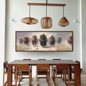 May include: A dining room featuring a long, dark wood table with matching chairs. Above the table hangs a framed painting of bison running through water. Three woven pendant lights are suspended from a wooden beam.